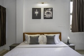 A hotel room with a bed, two pillows, a nightstand, a lamp, and two framed pictures on the wall. - Wandr Hotel HSR Layout Sector 7 (Bengaluru)
