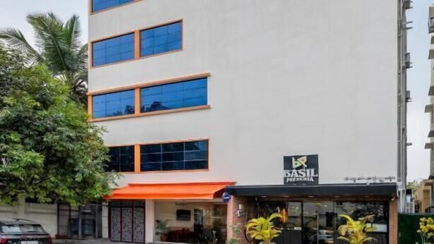 Un edificio de varios pisos con fachada plana, una entrada visible con toldo rojo y un letrero que indica restaurante o cafetería.