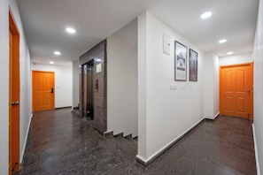 A corridor with a marble floor, a wall-mounted elevator, and two doors. - Wandr Hotel HSR Layout Sector 7 (Bengaluru)