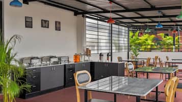 Un caffè moderno con angolo cottura, tavoli, sedie e vista sul verde attraverso ampie finestre.
