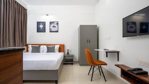Habitación de hotel con cama, escritorio, silla, armario, televisor y obras de arte en la pared.