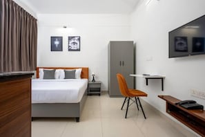 A hotel room with a bed, a desk, a chair, a wardrobe, a television, and artwork on the wall. - Wandr Hotel HSR Layout Sector 7 (Bengaluru)