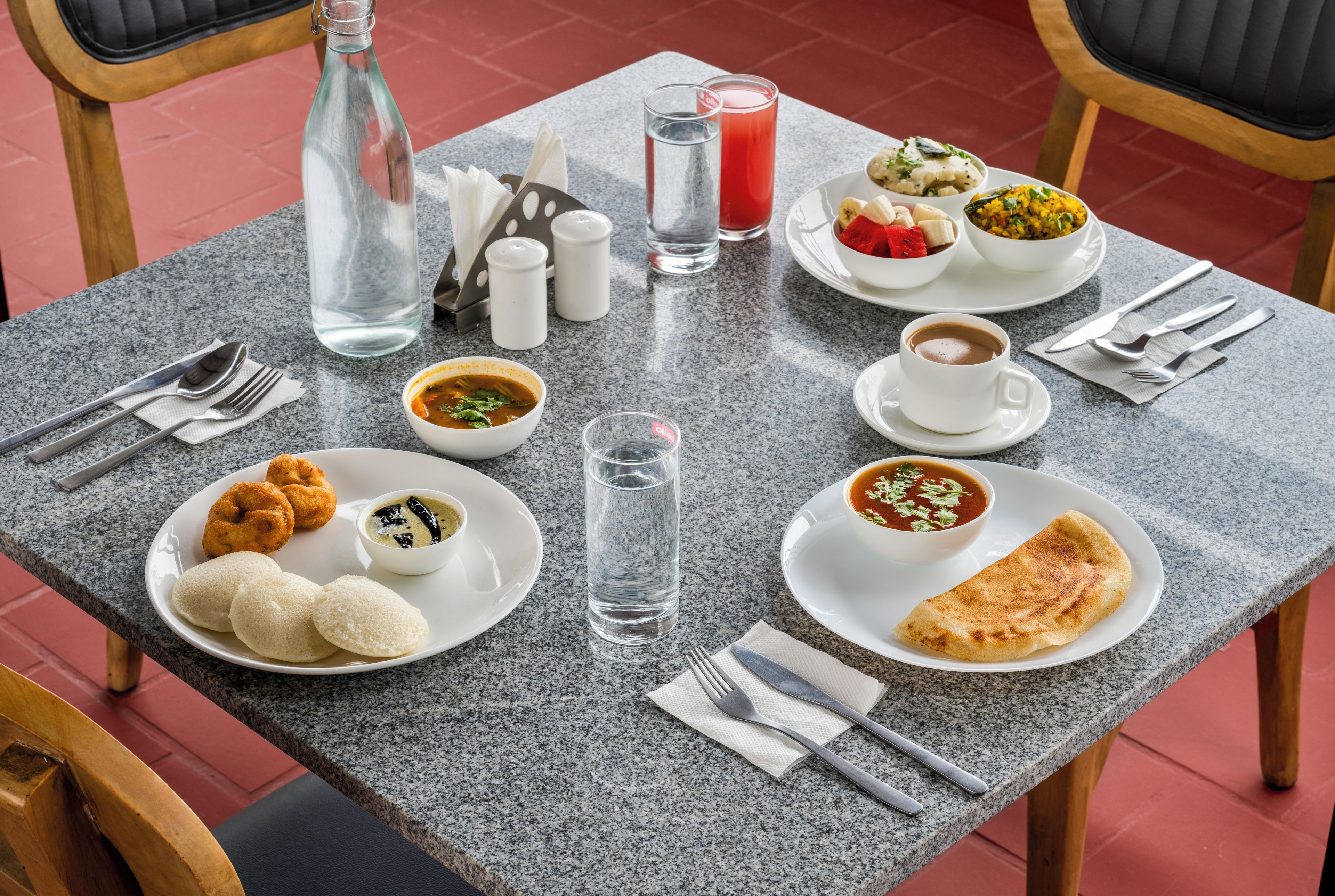 A dining table set with various dishes, including a bowl of soup, a plate of idlis, and a cup of coffee.