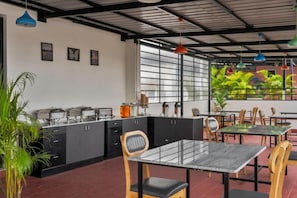 A restaurant with a black counter, wooden chairs, and a glass table. - Wandr Hotel HSR Layout Sector 7 (Bengaluru)
