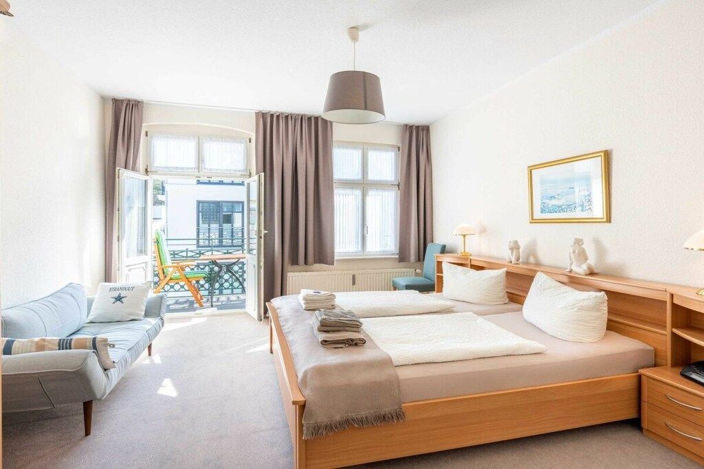 A hotel room with a bed, a sofa, a desk, a lamp, and a window with curtains.
