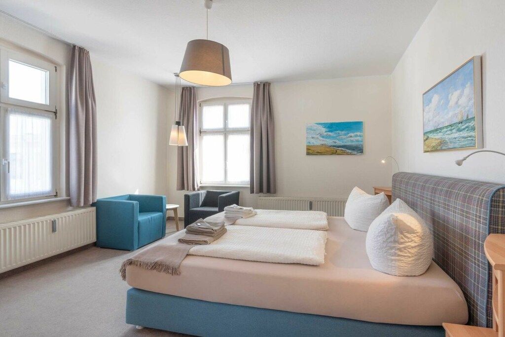 Una camera da letto con un letto, una sedia blu, una scrivania e un quadro appeso al muro.