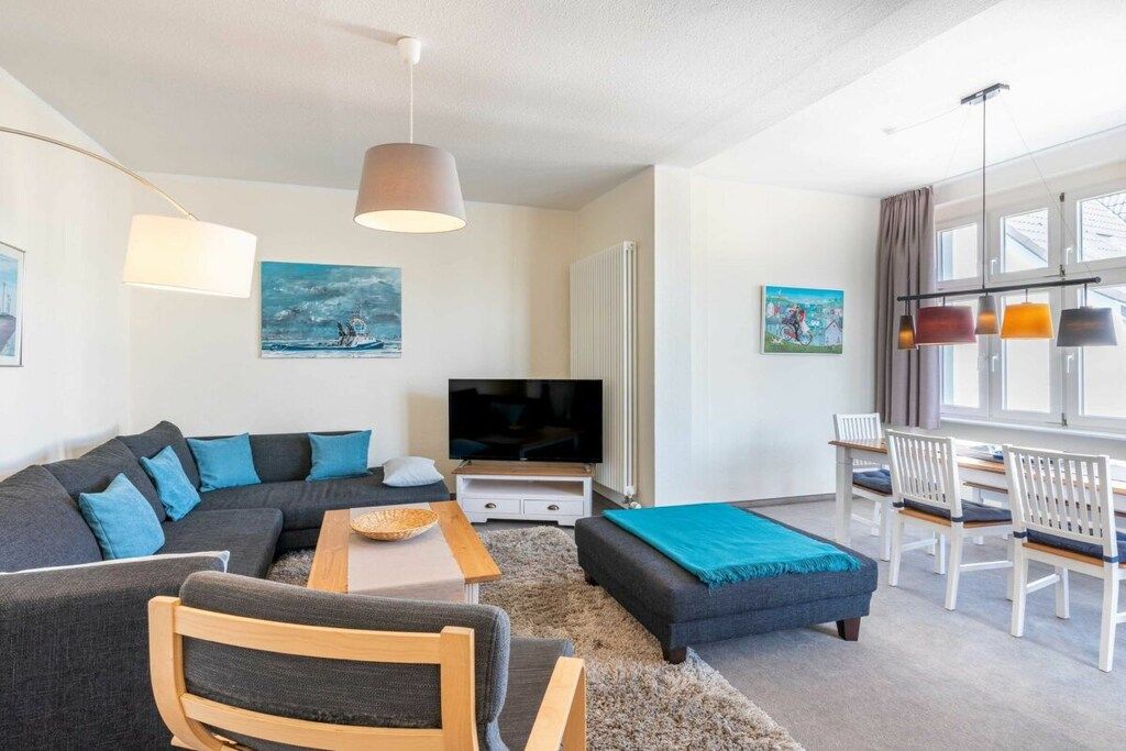 Ein modernes Wohnzimmer mit einer Eckcouch, einem Couchtisch, einem Fernseher und einem Essbereich mit Stühlen.
