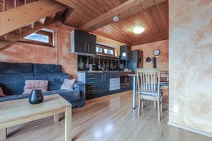 Un espacio habitable estilo loft acogedor, con techo de madera, una zona de cocina con electrodomésticos modernos y un comedor.
