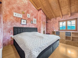 Ein Schlafzimmer mit einem großen Bett, Holzbalken an der Decke, einem Schreibtisch mit Schubladen und einem Fenster mit Blick.