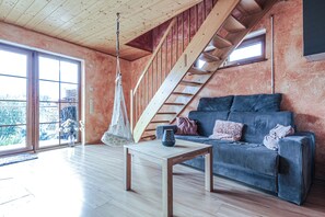 Ein großzügiger Wohnbereich mit einer Holztreppe, einem Hängesessel, einem Sofa mit gestreiften Kissen und einem Couchtisch.
