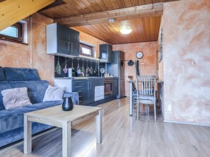 Um espaço de estar compacto com sofá, mesa de jantar, cozinha compacta e teto de madeira.