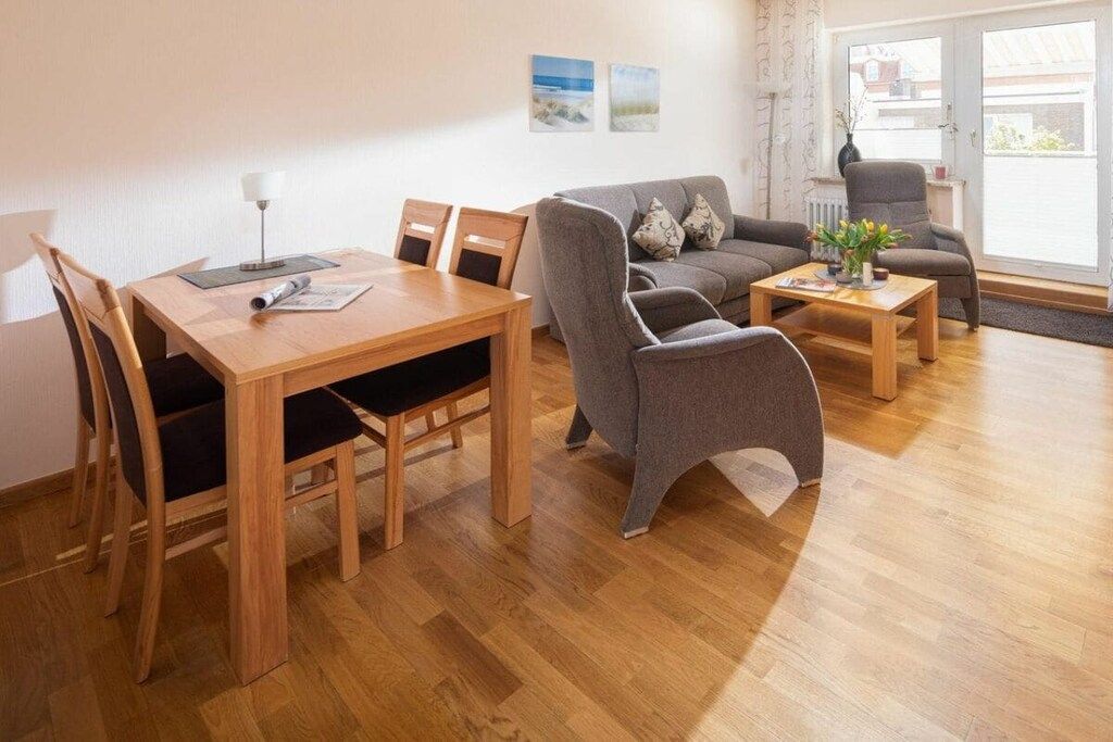 Ein Wohnzimmer mit einem Holzespeisetisch, zwei grauen Sofas und einem grauen Sessel.