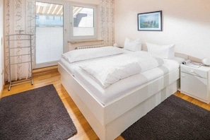 Ein Schlafzimmer mit Bett, Nachttisch, Heizkörper, Fenster und Tür.