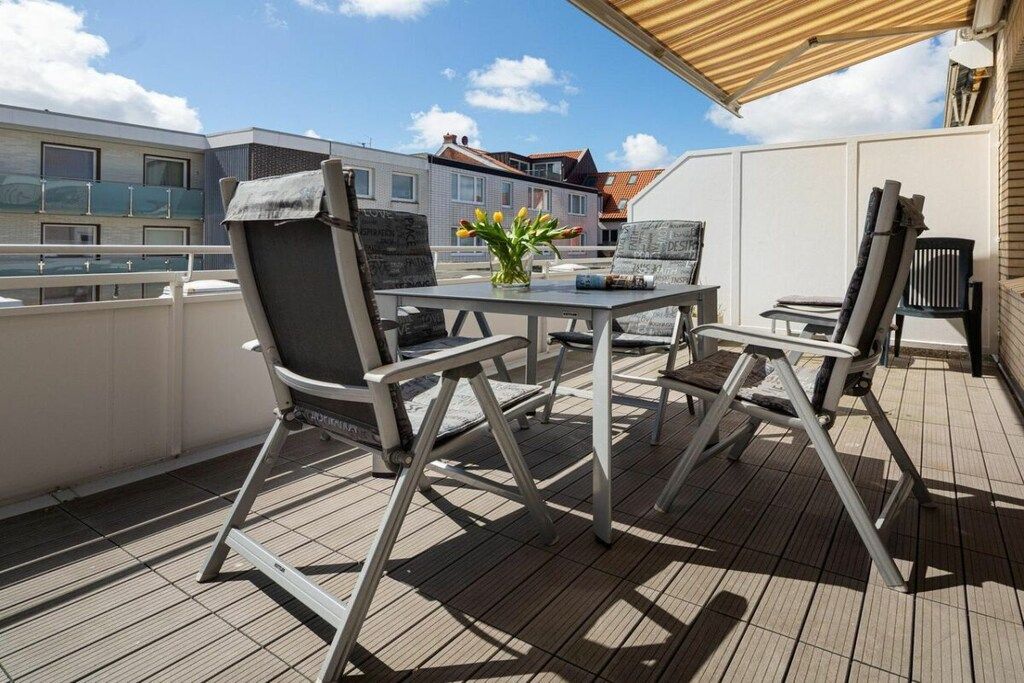 A balcony with a table and chairs, a small vase with flowers, and a view of buildings in the background.