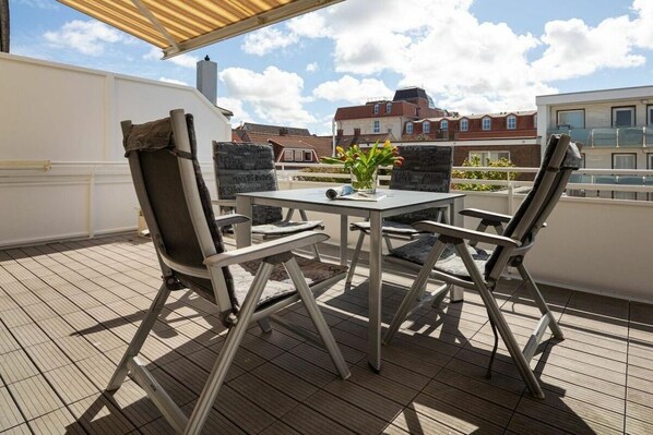 En tagterrasse med et bord, stole, en potteplante og udsigt til bygninger.