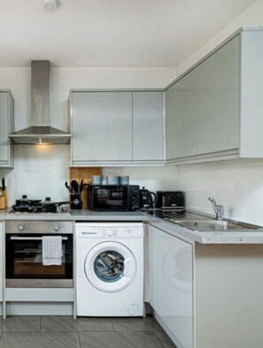 A compact kitchen with a built-in oven, microwave, and washing machine. -     Stay Soho | Stylish 2BR Steps from the West End (London)