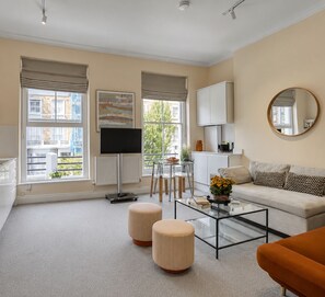 A modern living room with a sofa, ottomans, a coffee table, and a television. -     Stay Soho | Stylish 2BR Steps from the West End (London)