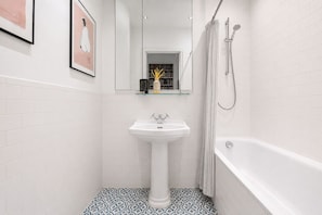 A bathroom with a white pedestal sink, a bathtub, and a shower. -     Stay Soho | Stylish 2BR Steps from the West End (London)