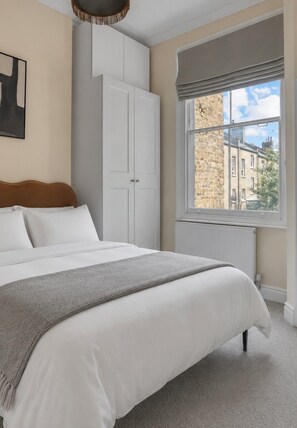A bedroom with a bed, a wardrobe, a window with a view of buildings, and a radiator. -     Stay Soho | Stylish 2BR Steps from the West End (London)