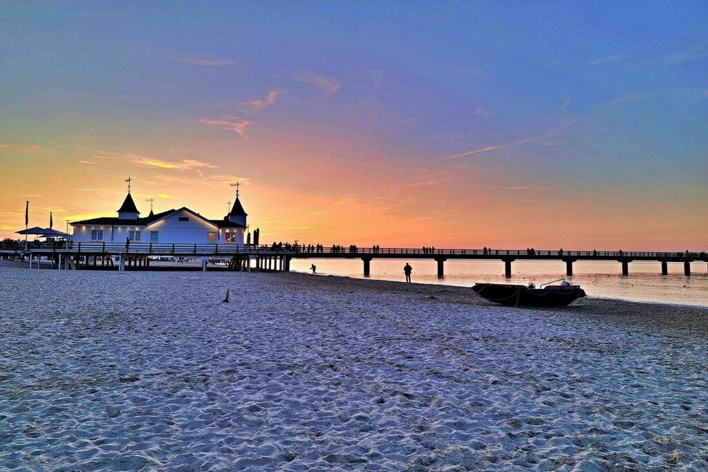 A beach with a pier extending into the water, a boat, and a building with a cross on top.