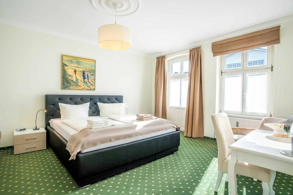 Een hotelkamer met een bed, bureau, stoel, lamp, schilderij en een raam met gordijnen.