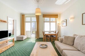 Un salon comprenant un téléviseur, une table basse en bois, un canapé, une table à manger avec des chaises et une grande fenêtre avec des rideaux.