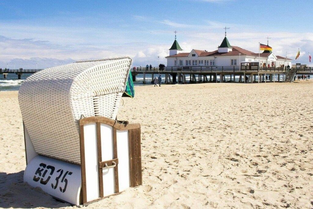 A beach with a white beach chair labeled 'BC35' and a pier with buildings in the background.