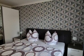 Una camera da letto con una parete decorata, un letto con copripiumino fantasia, due cuscini, un comodino e una lampada.