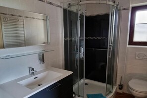 Un bagno moderno con doccia vetro, lavandino bianco e water.