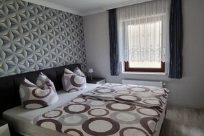 A bedroom with a patterned wall, a bed with circular-patterned bedding, a nightstand, and a window with curtains. - Franzi holiday apartment (Ahlbeck (Seebad))