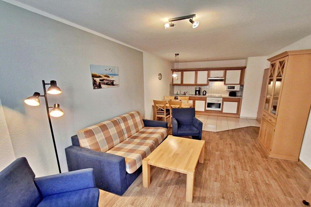 A compact living space with a sofa, two armchairs, a coffee table, a dining area with chairs, and a kitchen with cabinets.