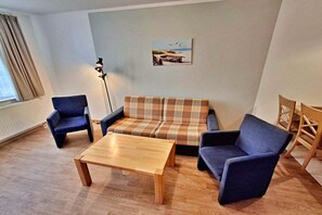 Ein Wohnzimmer mit einer Couch, zwei Sesseln, einem Couchtisch, einer Stehlampe und einem Bild an der Wand.