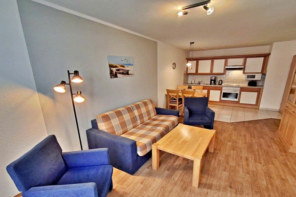 Ein Wohnzimmer mit einer Couch, zwei Sesseln, einem Holztisch und einem Essbereich mit Tisch und Stühlen.