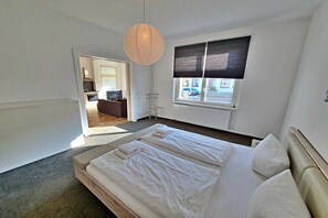 Un dormitorio con una cama grande, una ventana con persianas, un radiador y una lámpara colgante.