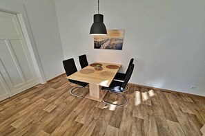 Ein Essbereich mit einem Holztisch, vier Stühlen, einer Pendelleuchte und einem an der Wand hängenden Bild.