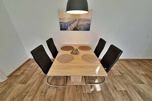 A dining table with four chairs, a pendant light, and a painting above. - Holiday apartment with 1 bedroom (Ahlbeck (Seebad))