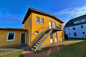 A yellow building with a staircase leading to a balcony, a door, and a window. - Holiday apartment with 1 bedroom (Ahlbeck (Seebad))