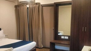 Una habitación de hotel con cama, banca, armario y unidad de aire acondicionado.