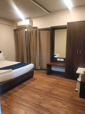 A hotel room with a bed, a bench, a wardrobe, and an air conditioning unit. - Hotel Blue Pearl (Bengaluru)
