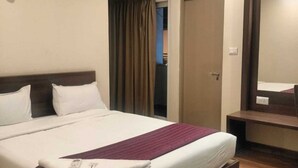 Habitación de hotel con una cama, una mesita de noche, un espejo, un equipo de aire acondicionado y una puerta.