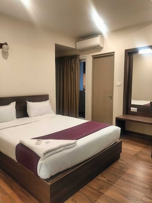 A hotel room with a bed, a bedside table, a mirror, an air conditioning unit, and a door. - Hotel Blue Pearl (Bengaluru)