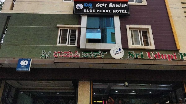 Un edificio de varios pisos con un letrero que dice 'Blue Pearl Hotel' y un letrero que dice 'Sri Udupi Palace'.