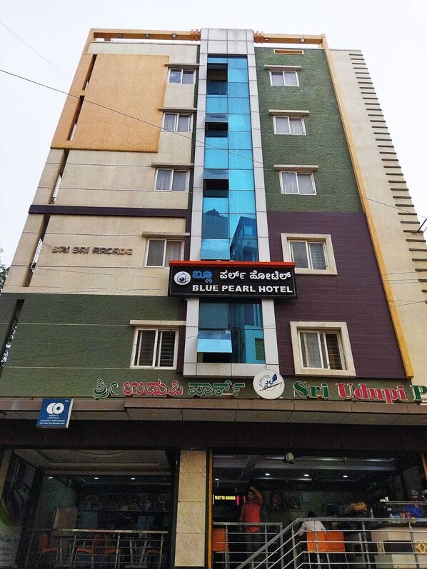 A multi-story building with a sign for 'Blue Pearl Hotel' and a sign for 'Sri Udupi Palace.' - Hotel Blue Pearl (Bengaluru)