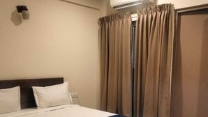 Una habitación de hotel con una cama grande, aire acondicionado, piso de madera y una cortina.