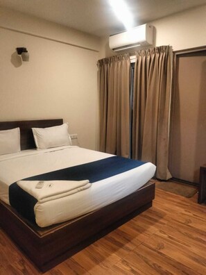 A hotel room with a large bed, an air conditioning unit, a wooden floor, and a curtain. - Hotel Blue Pearl (Bengaluru)