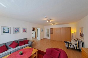 Ein großzügiger Wohnbereich mit einer Couch, Sesseln, einem Couchtisch und einem Esstisch. Holzschränke und ein Kleiderschrank sind ebenfalls vorhanden.