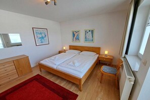 Ein Schlafzimmer mit einem hölzernen Bett, einem roten Teppich, einer Holzkommode und zwei gerahmten Kunstwerken an der Wand.