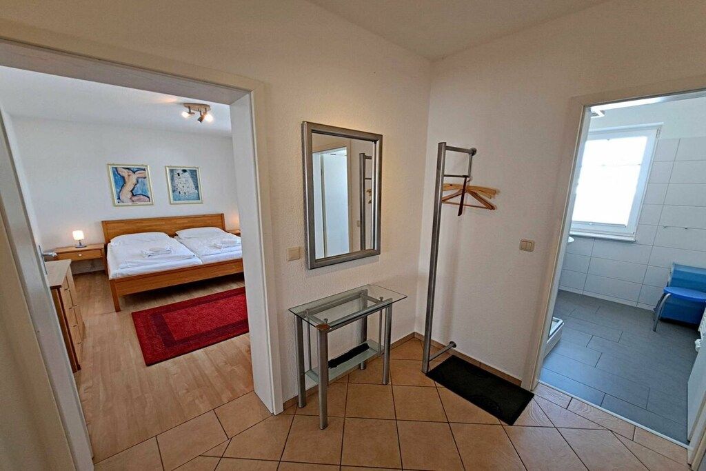 A bedroom with a bed, a bedside table, a mirror, and a red rug.