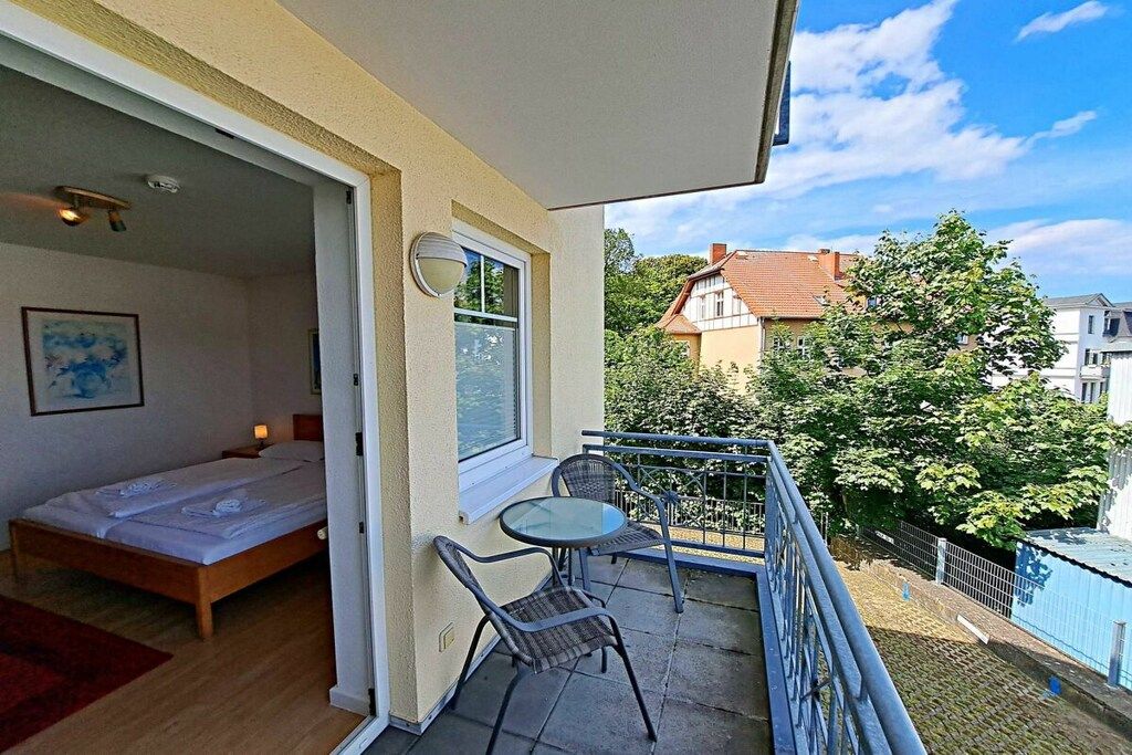 Een balkon met een bed, een tafeltje en stoelen, met uitzicht op een tuin en gebouwen.