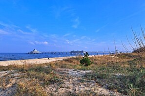 Un paysage côtier avec une jetée qui s’avance dans la mer, une plage de sable et une végétation clairsemée.